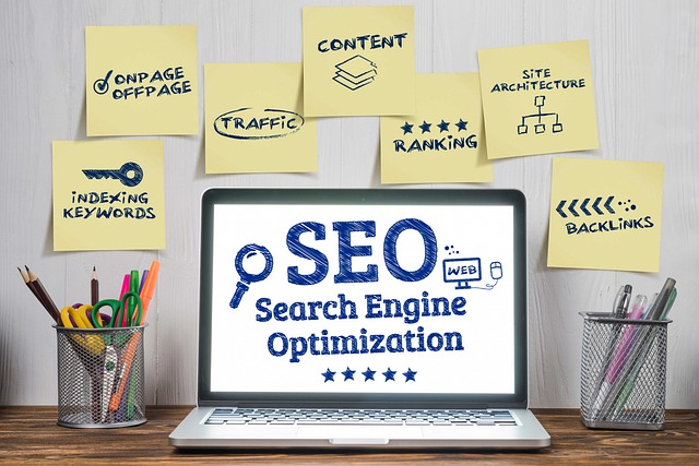 Laptop auf einem Tisch. Auf dem Bildschirm steht SEO Search Engine Optimization. An der Wand über dem Laptop kleben Post-Its mit INDEXING KEYWORDS, ONPAGE/OFFPAGE,TRAFFIC, CONTENT, RANKING, SITE ARCHITECTURE und BACKLINKS